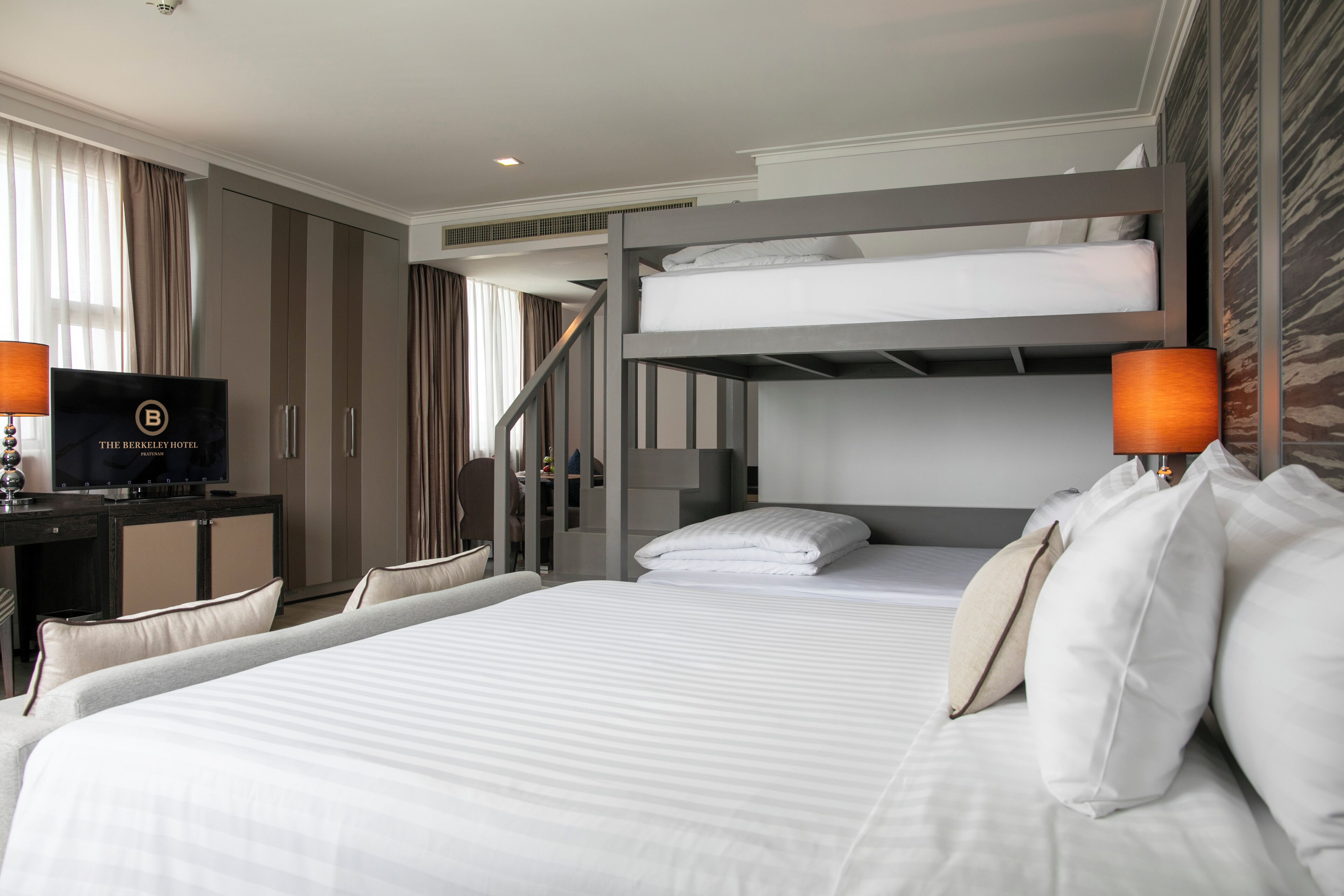 Una habitación de hotel con literas, un escritorio y un televisor, y una escalera.
