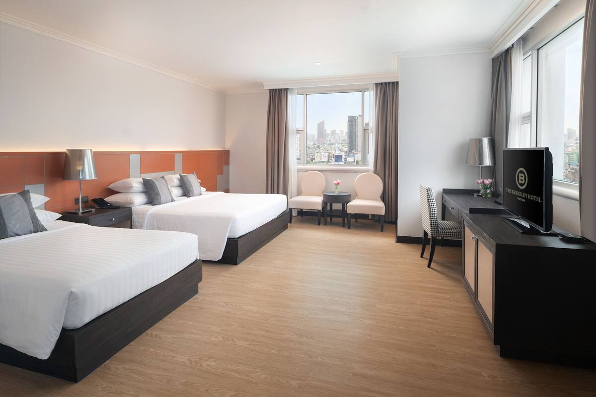 A hotel room with two beds, a desk with a TV, a chair, and a view of the city.