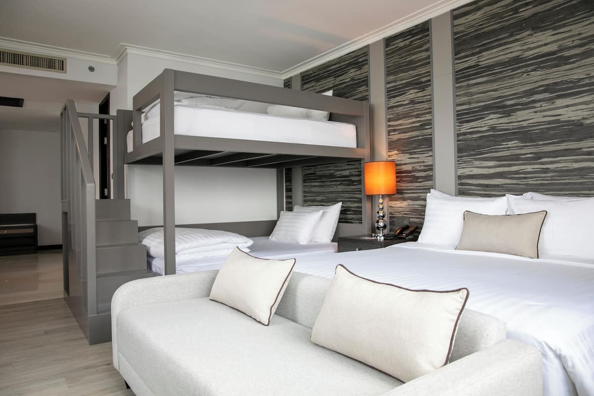 A hotel room with a bunk bed, a sofa, a nightstand with a lamp, and a textured wall.