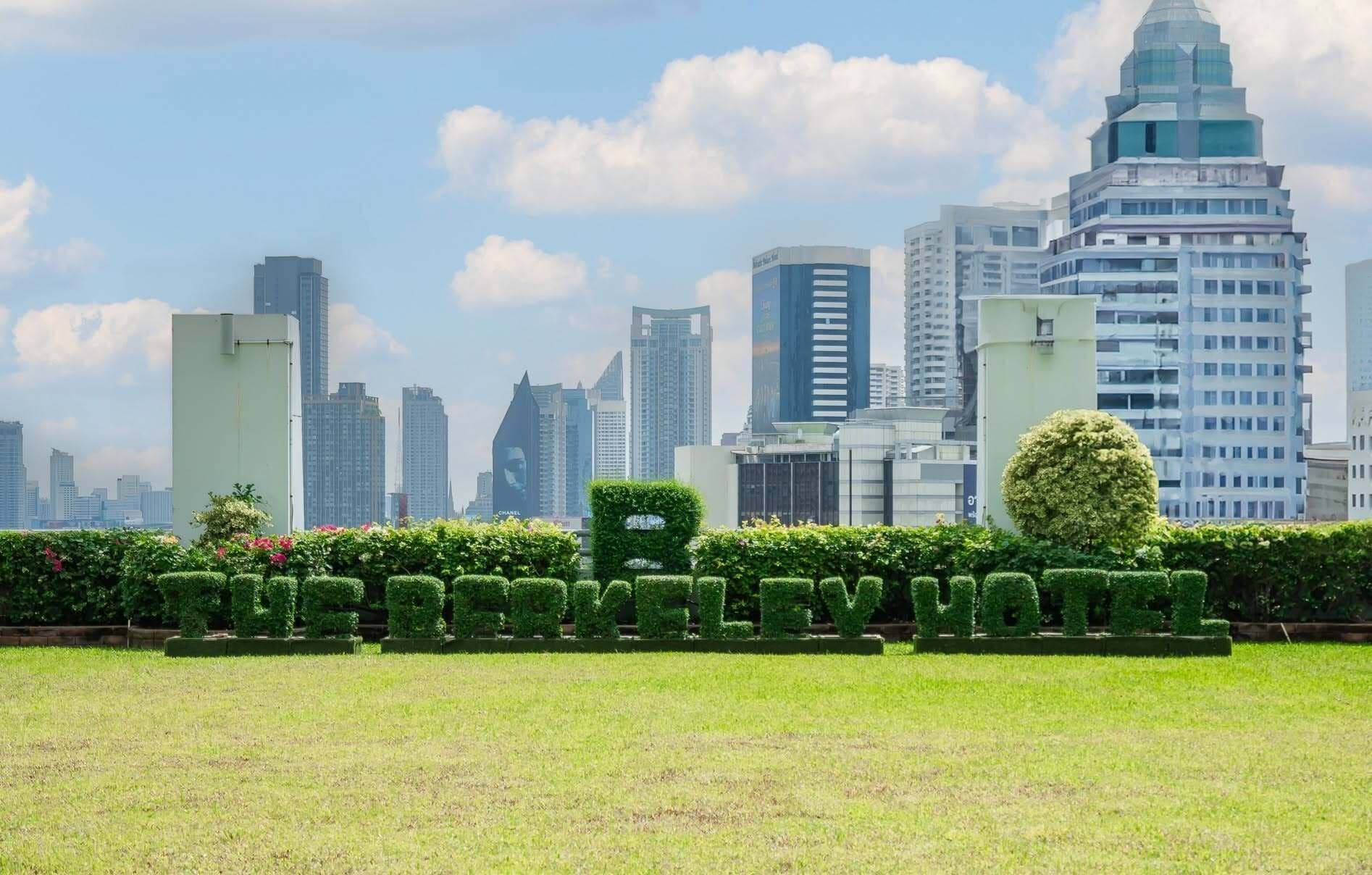 A cityscape with modern high-rise buildings and a well-maintained park area with neatly trimmed hedges.