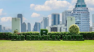 A cityscape with modern high-rise buildings and a well-maintained park area with neatly trimmed hedges.