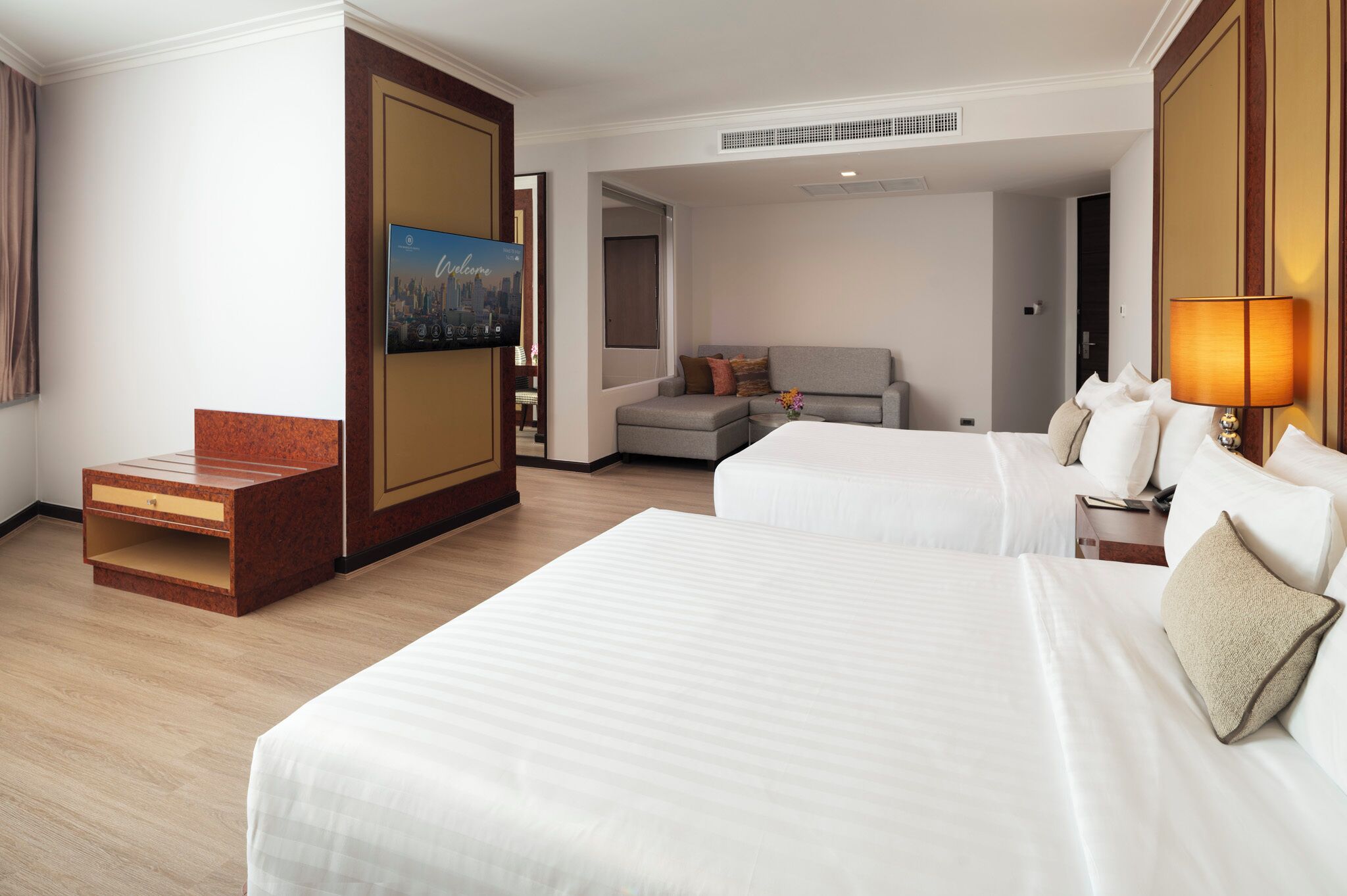 A hotel room with two beds, a sofa, a TV, and a wooden cabinet.