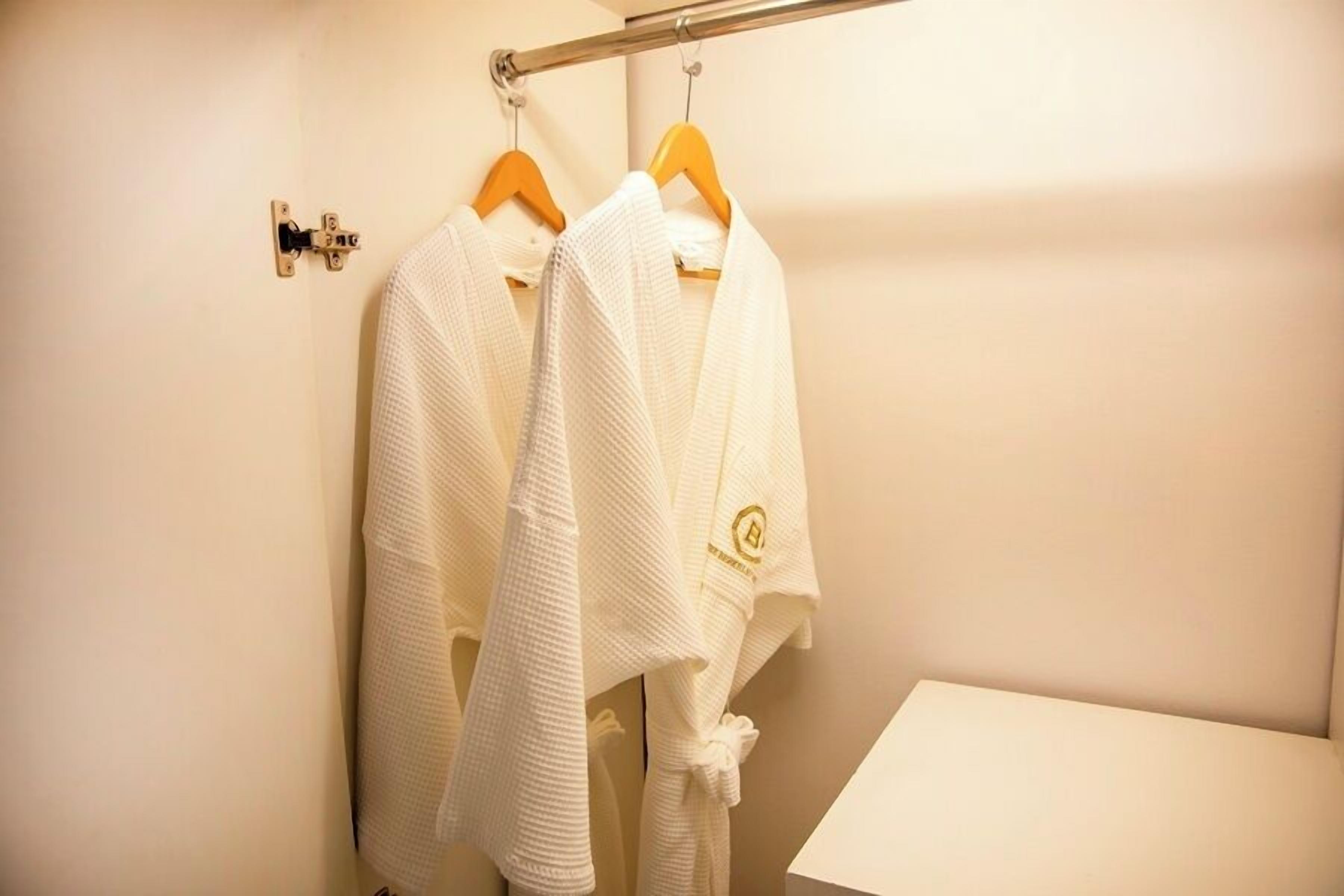 Un baño con dos albornoces blancos colgados en un perchero, un perchero para toallas y un lavamanos pequeño y blanco.