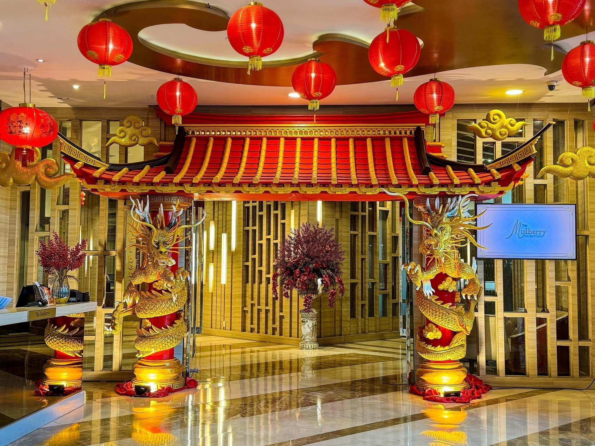 A hotel lobby with a traditional Chinese architectural entrance, red lanterns, and golden dragon statues.