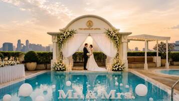 A wedding ceremony with a couple under an arch by a pool with floating spheres.