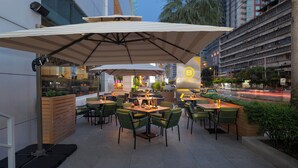 Een terras met tafels en stoelen, parasols en uitzicht op een drukke straat.