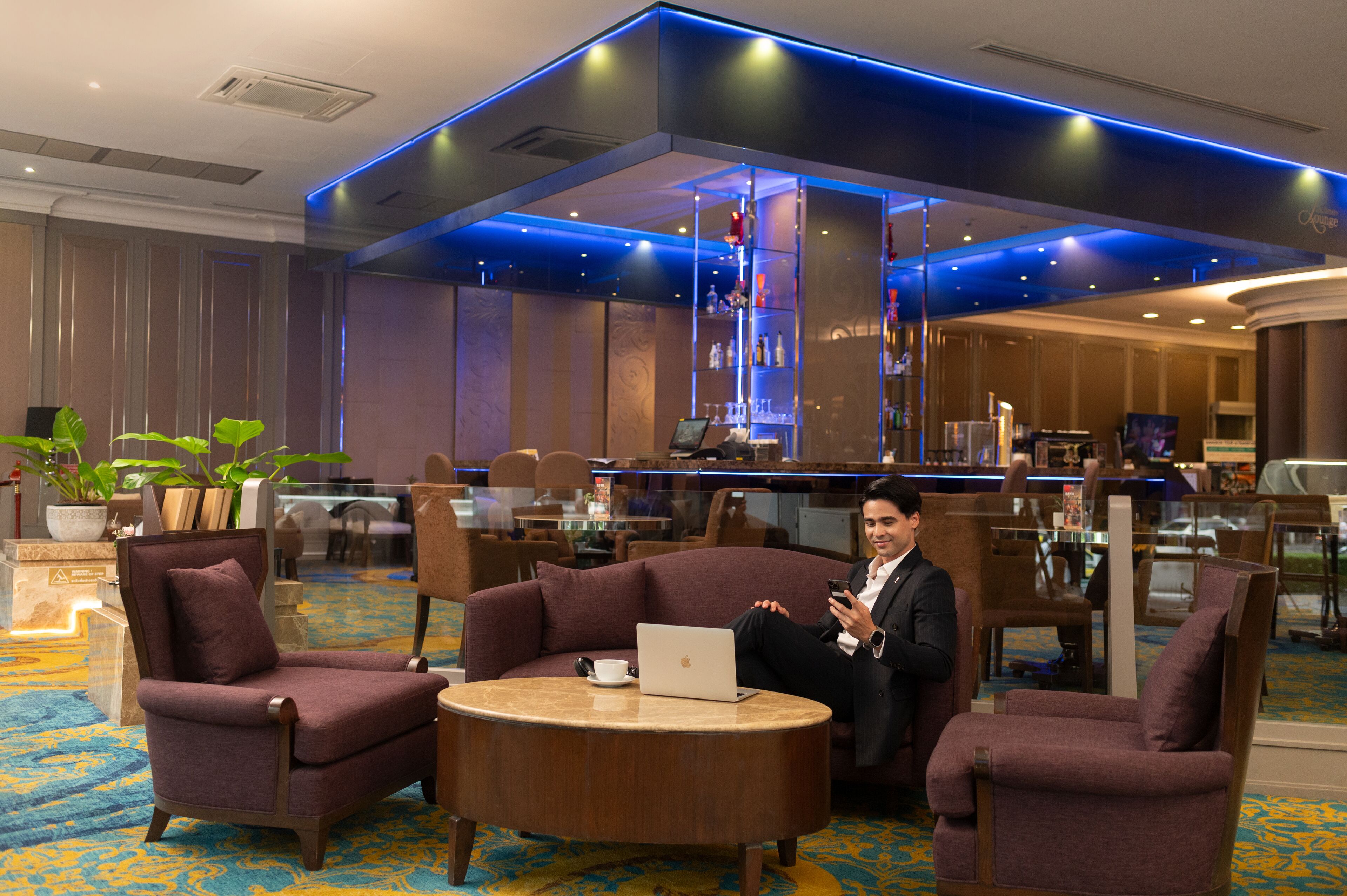 A modern hotel lobby with a bar area, seating arrangements, and a large plant.