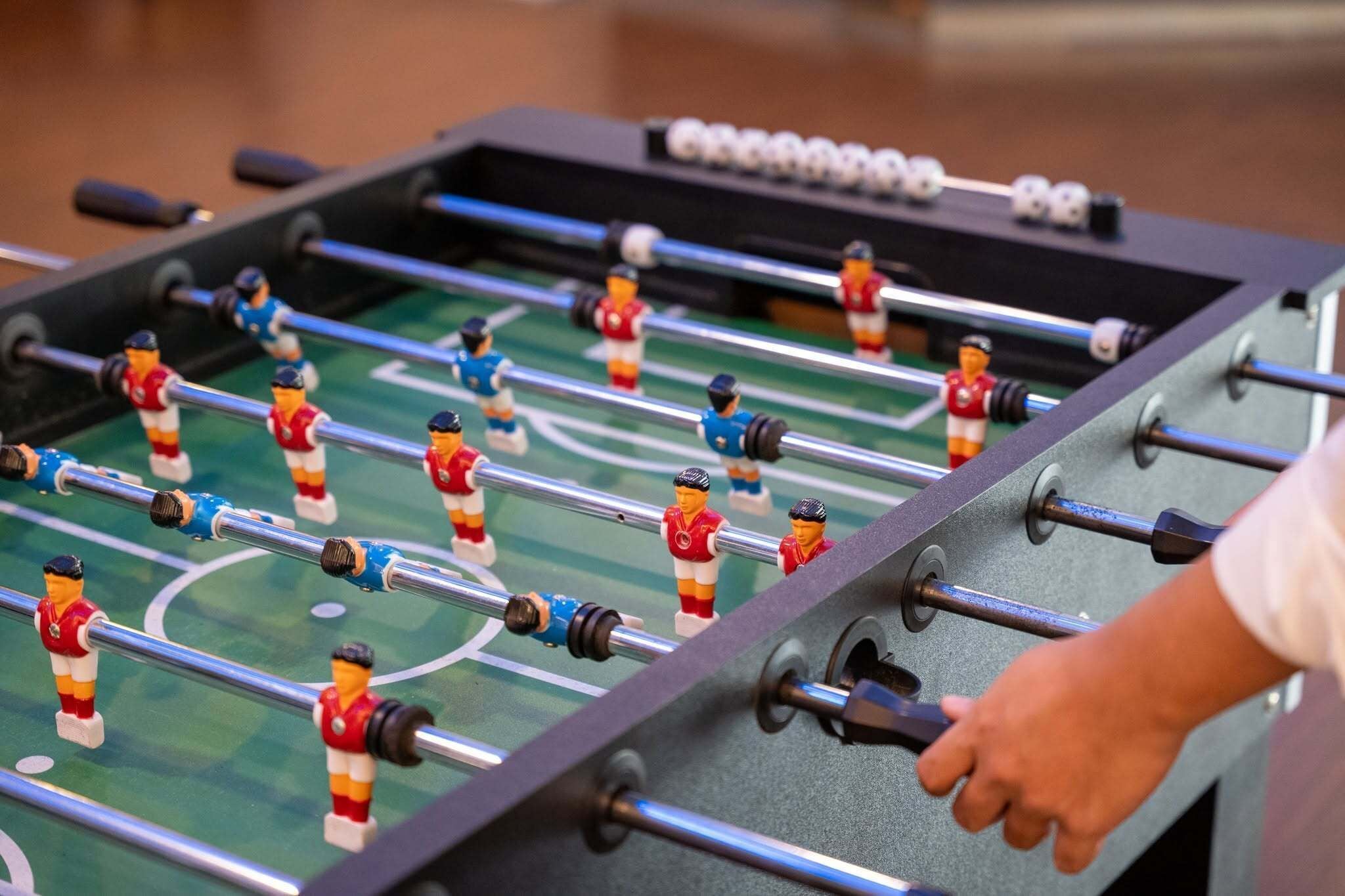 Ein Kicker mit zwei Mannschaften, eine in Rot und eine in Blau, und eine Hand, die die Stangen justiert.