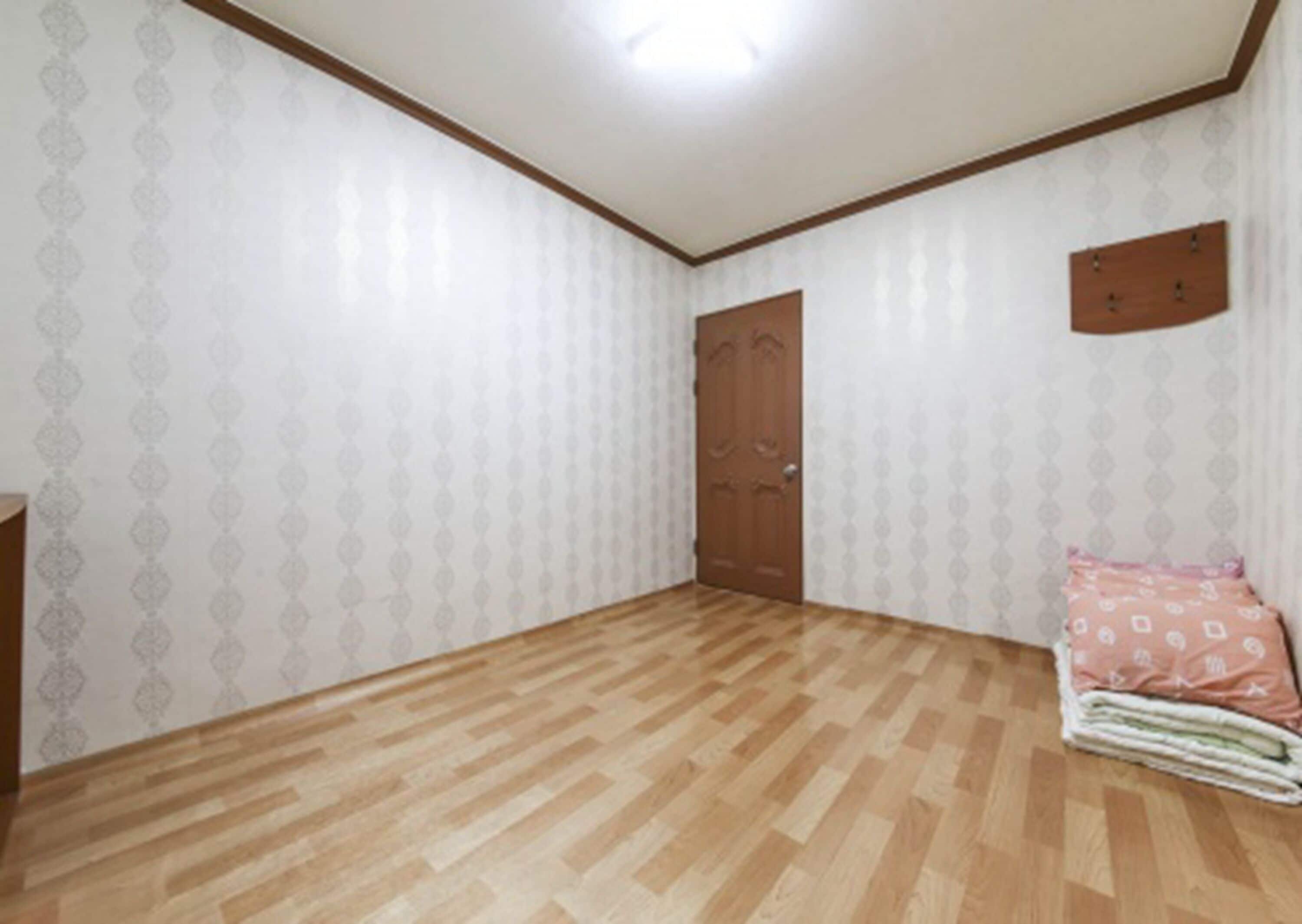 A room with patterned wallpaper, a wooden door, and a small bed with a pink blanket.