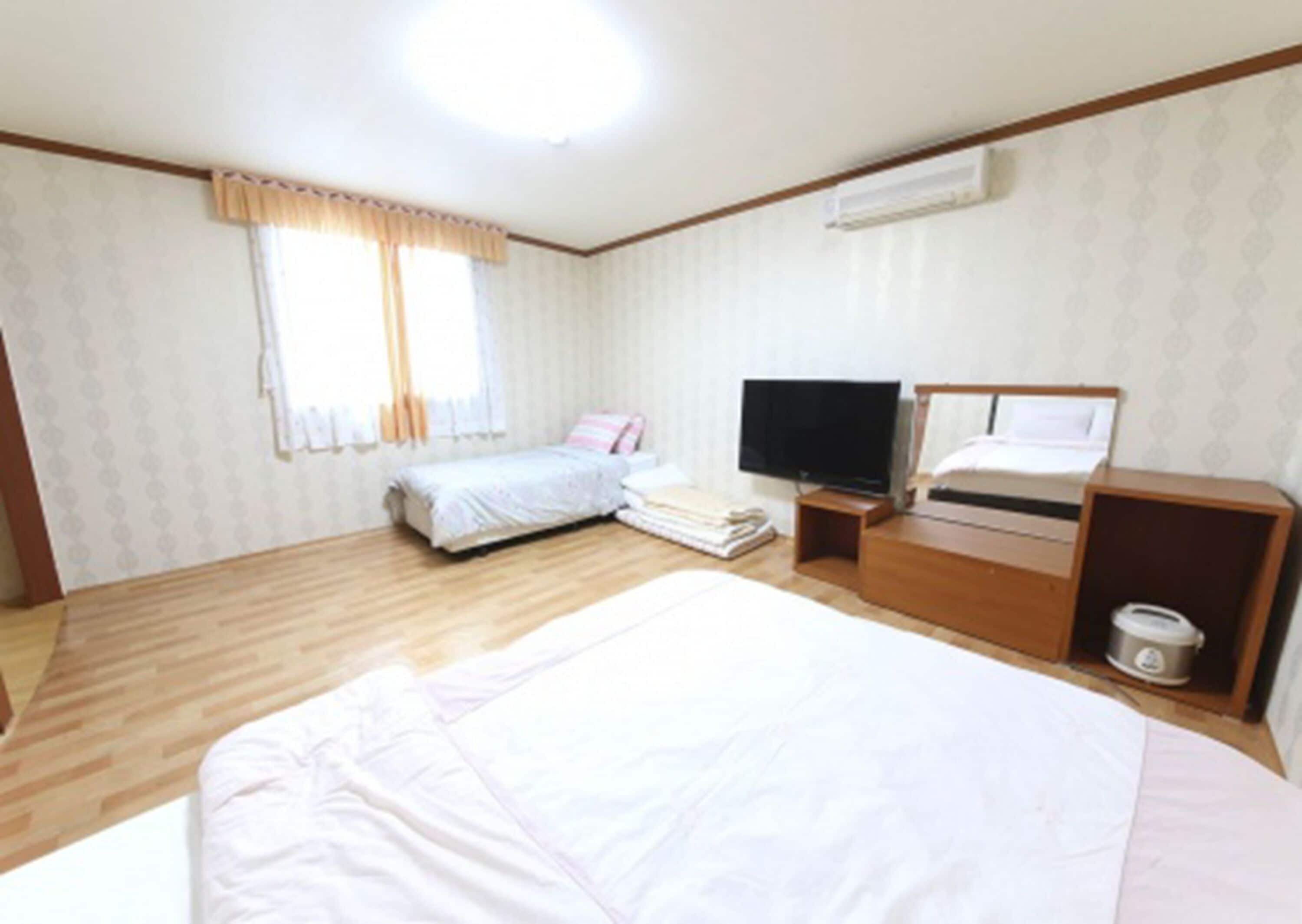 A bedroom with a large bed, a smaller bed, a TV, and a desk with a computer.
