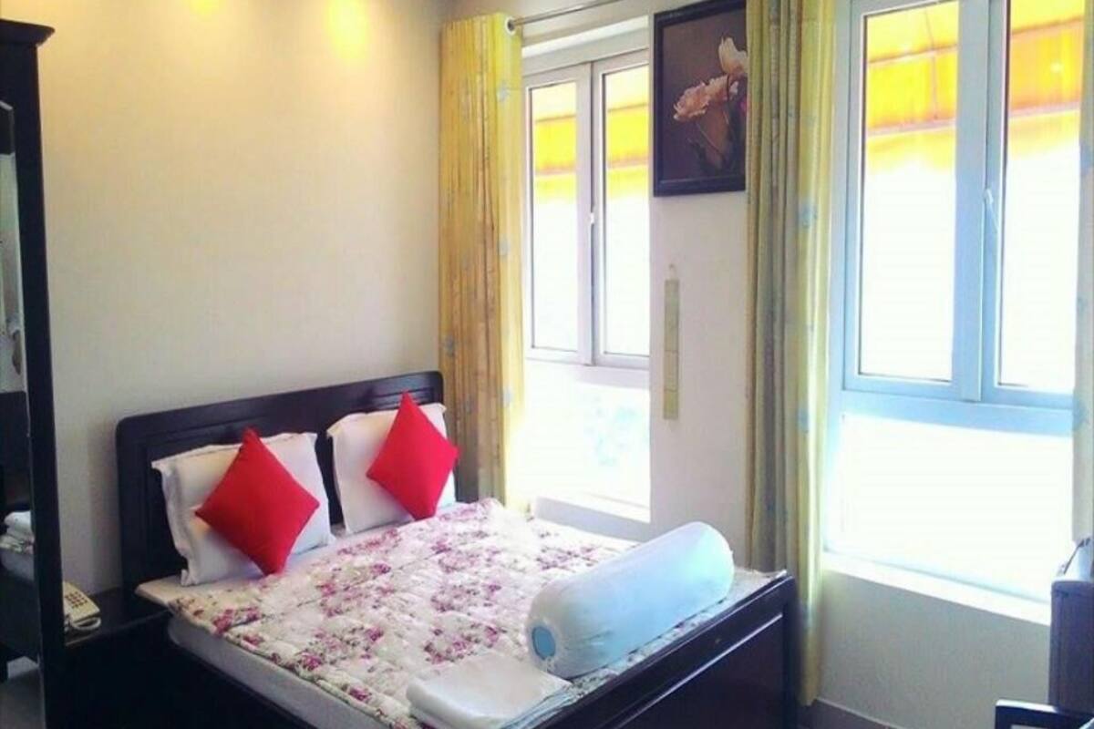 Un dormitorio con una cama, una mesita de noche, una ventana con cortinas y un cuadro en la pared.