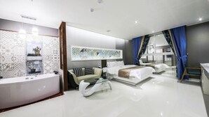 Quarto de hotel moderno com uma cama grande, um sofá, uma mesa de centro de vidro, uma penteadeira com espelho e banheiro com banheira.
