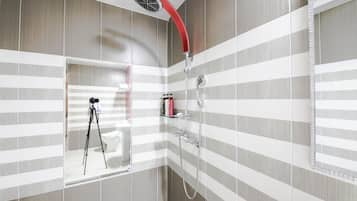 Un baño moderno con paredes de azulejos a rayas, una ducha con manguera roja y una cámara montada en un trípode.