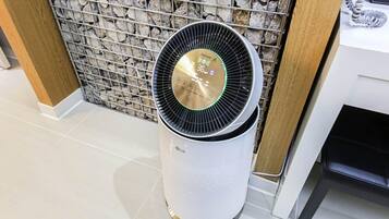 A white LG air purifier with a digital display, placed against a stone wall and a white tiled floor.