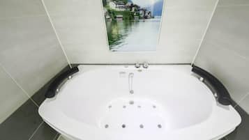 A modern bathroom with a large bathtub, a view of a lake with buildings, and tiled walls.