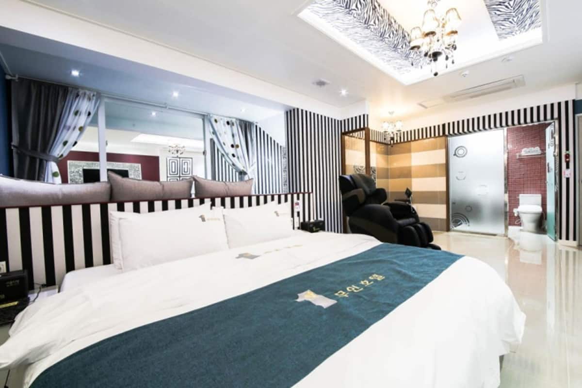 Habitación de hotel moderna con una cama grande, una silla de masaje y vistas a la ciudad.