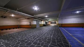 A spacious indoor parking area with a patterned floor, overhead lighting, and safety railings along the walls.