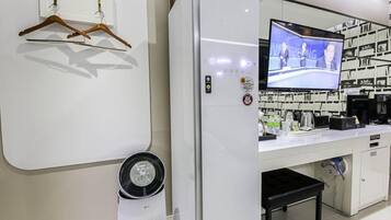 Una tienda minorista moderna con un televisor de pantalla plana mostrando un noticiero, una barra blanca con varios productos y un ventilador fijado a la pared.