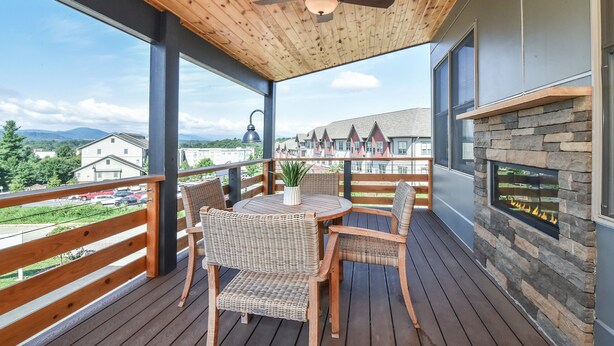 Un terrazzo in legno con un tavolo rotondo e sedie in vimini, affacciato su un panorama suggestivo di edifici e montagne.