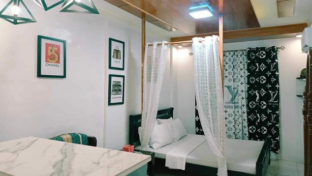 A bedroom with a bed, a bedside table, a vanity with a mirror, and a hanging light fixture. - FABULUZ SIGNATURE STUDIO at Princess Place (Malolos)