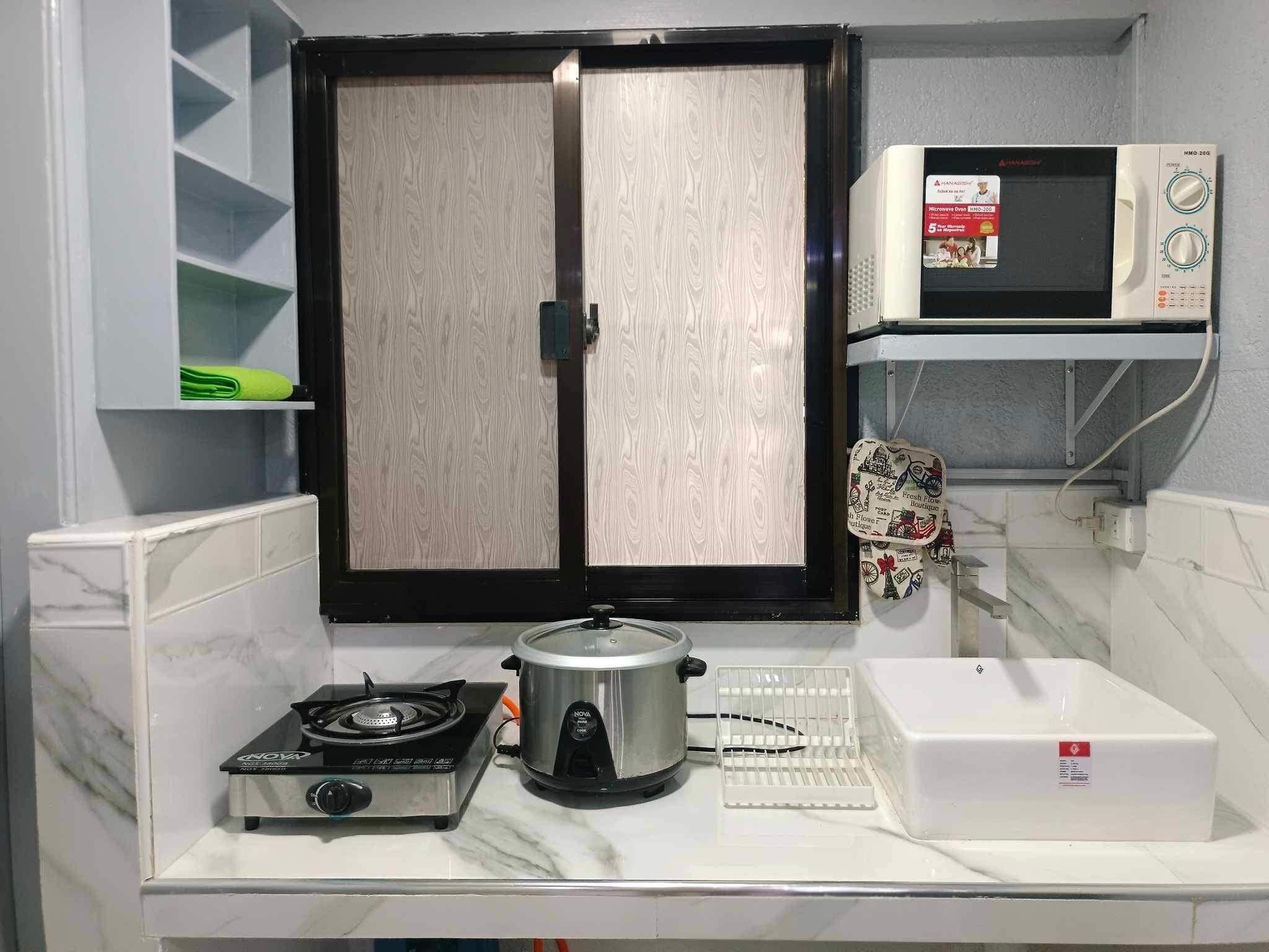 Cozinha com fogão, panela de cozimento lento, micro-ondas e armário branco com janela.