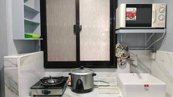 Cozinha com fogão, panela de cozimento lento, micro-ondas e armário branco com janela.