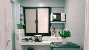 A compact kitchen with a gas stove, microwave, and a refrigerator. - FABULUZ SIGNATURE STUDIO at Princess Place (Malolos)