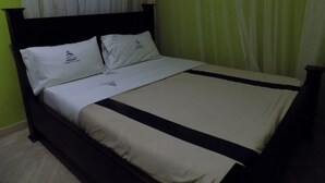 Una cama bien tendida con cabecera negra, ropa de cama blanca y un logo en las almohadas.