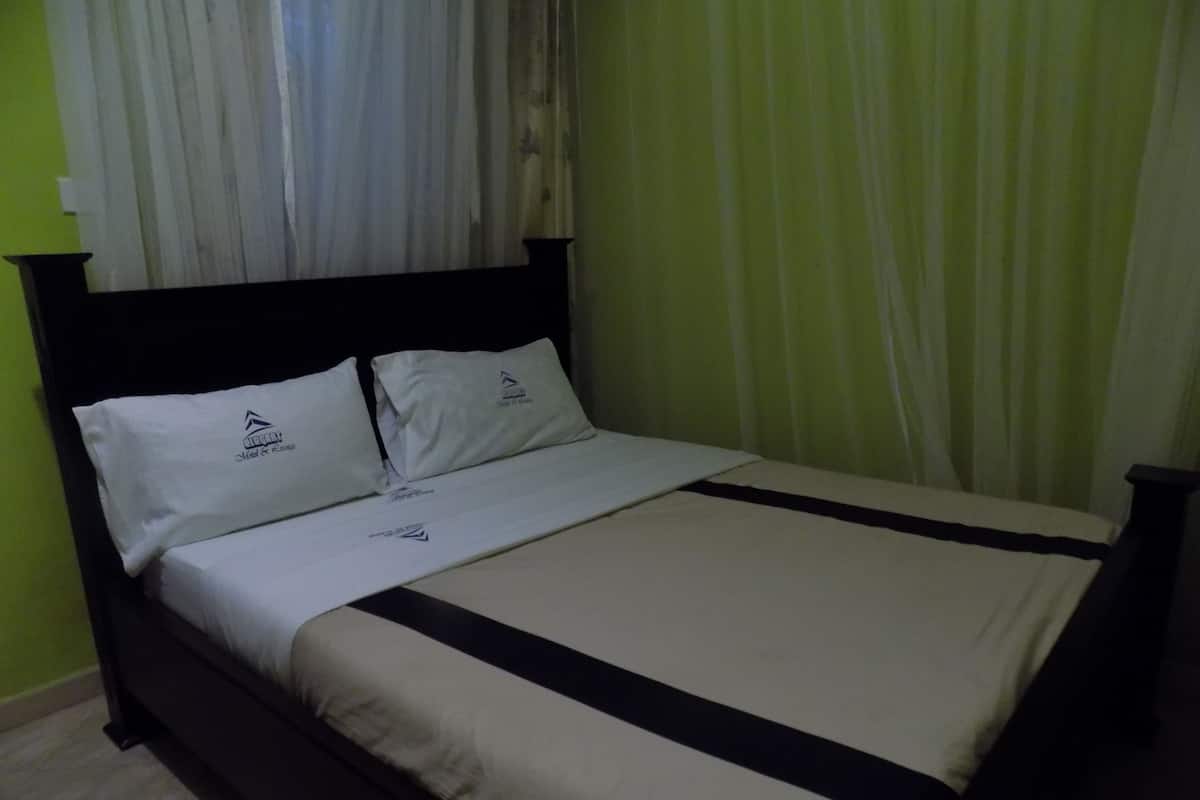 A neatly made bed with a black headboard, white bedding, and a logo on the pillows.