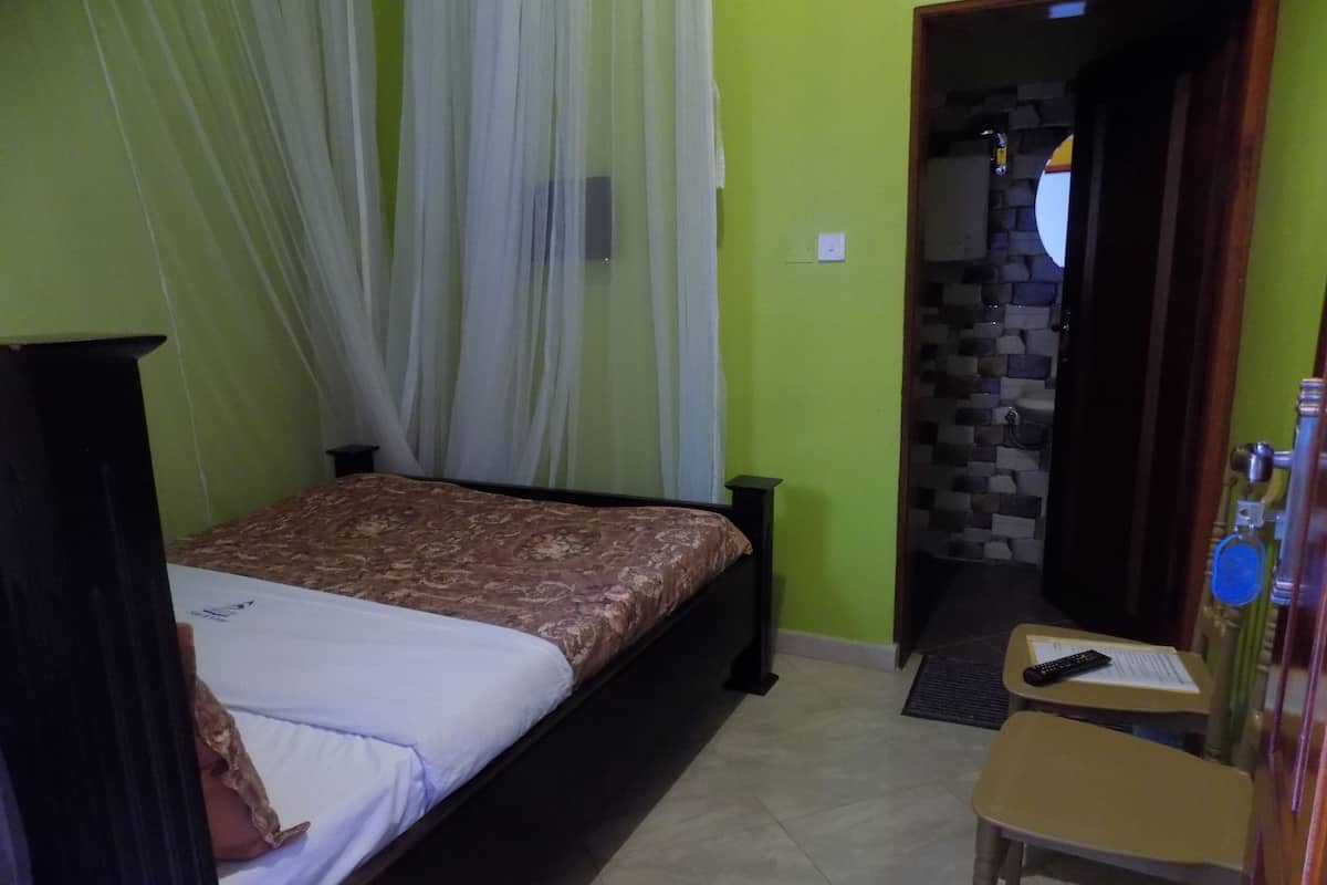 A bedroom with a bed, a chair, a desk, and a bathroom visible through an open door.