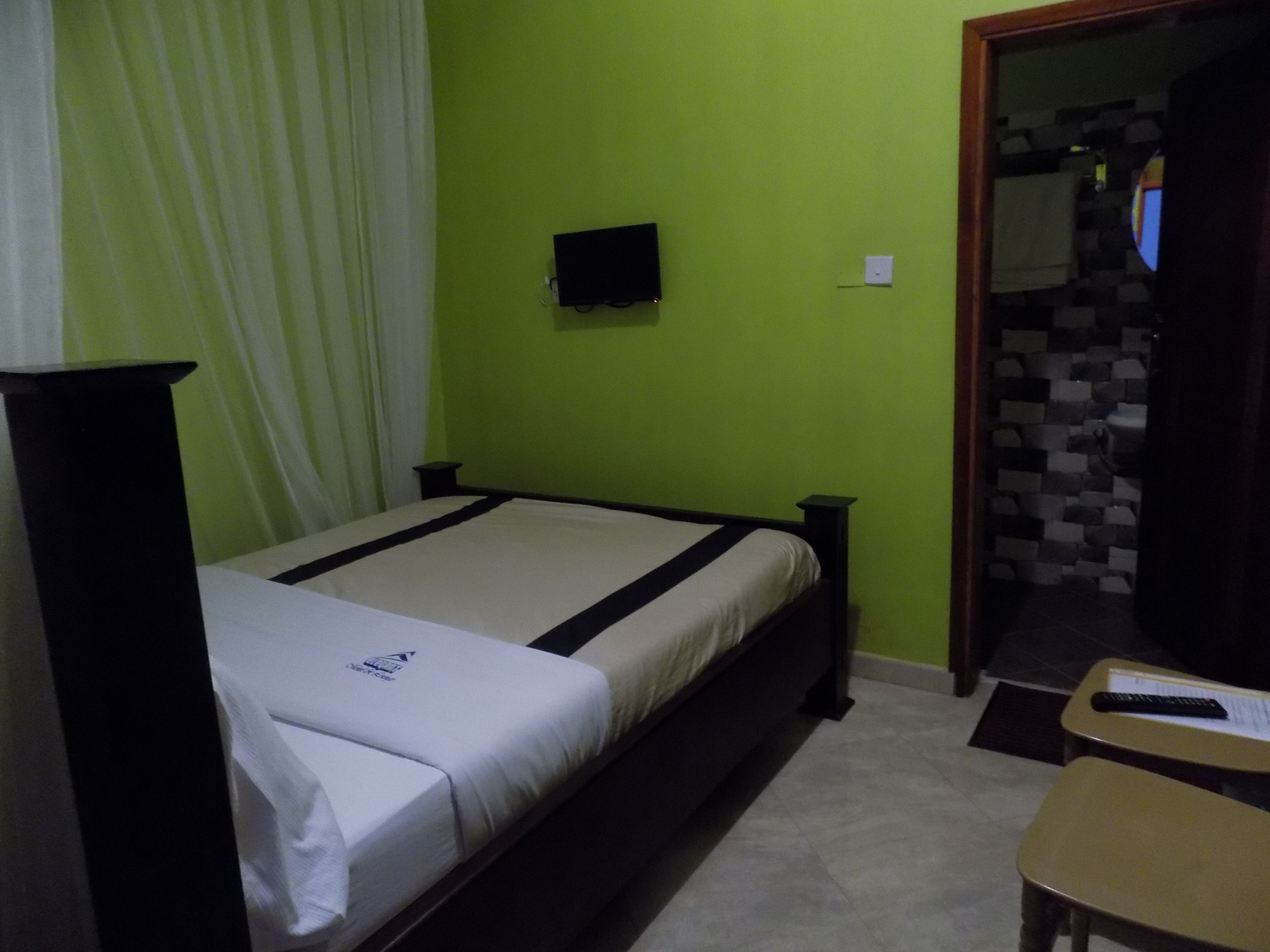 Una habitación con cama, una mesita, televisión y baño visible a través de una puerta abierta.
