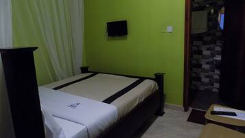 Una habitación con cama, una mesita, televisión y baño visible a través de una puerta abierta.