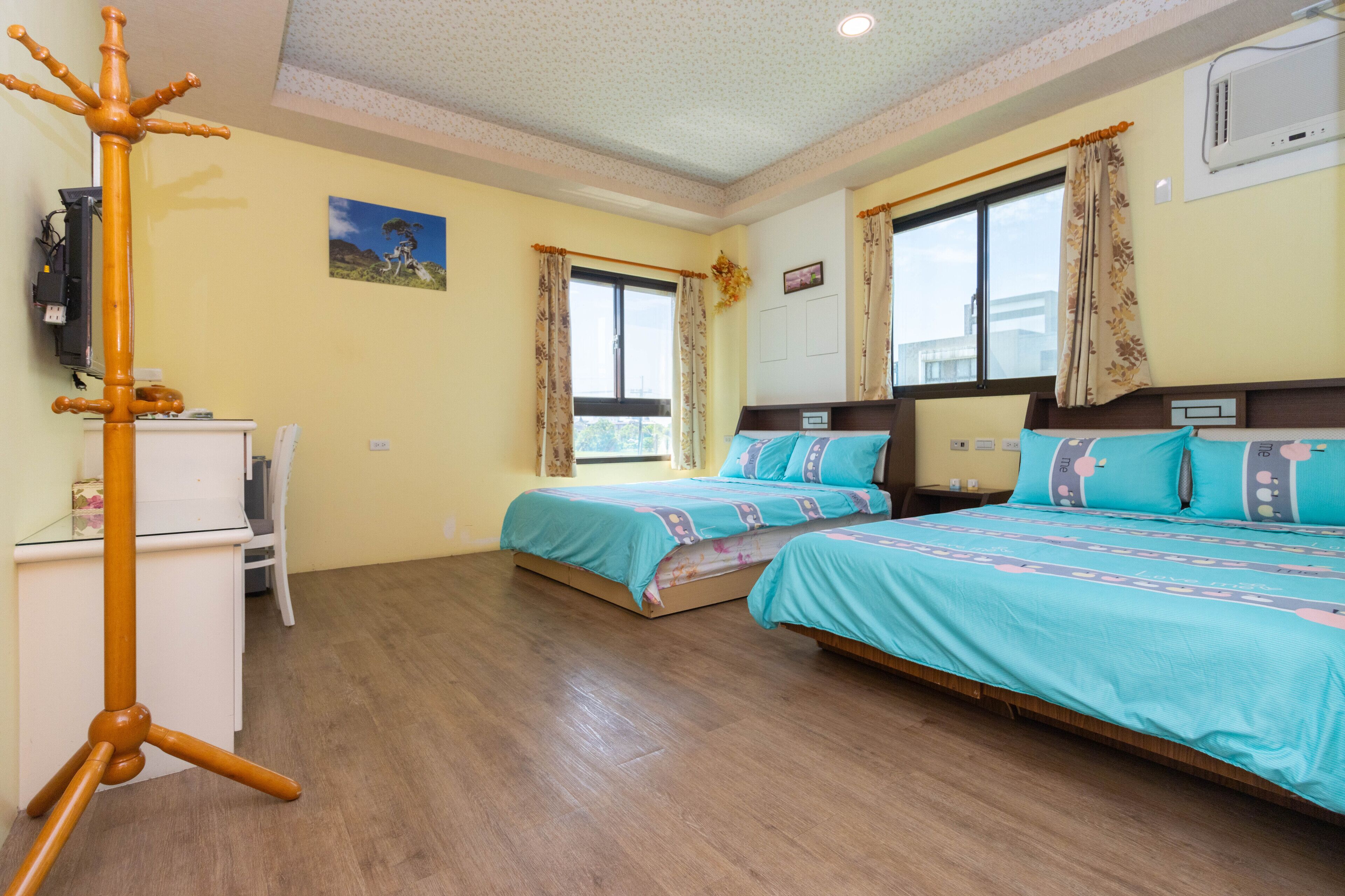 A hotel room with two beds, a desk, a television, and a window with curtains.