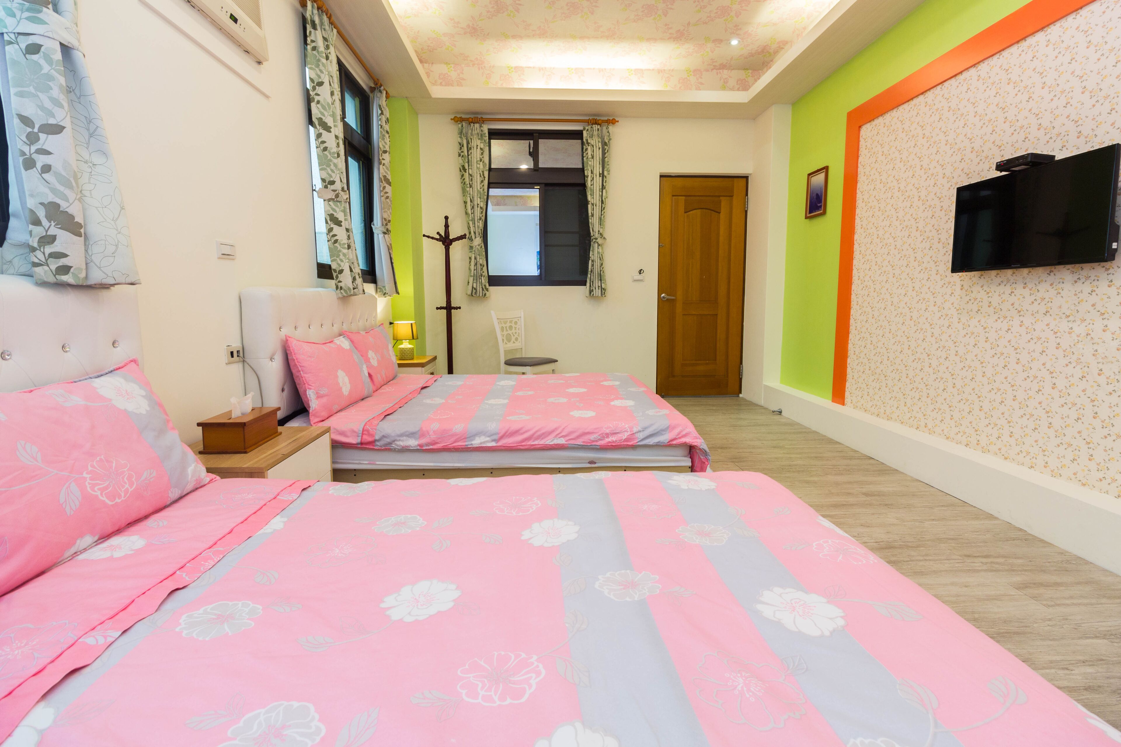 A bedroom with two beds, a television, and a window with curtains.