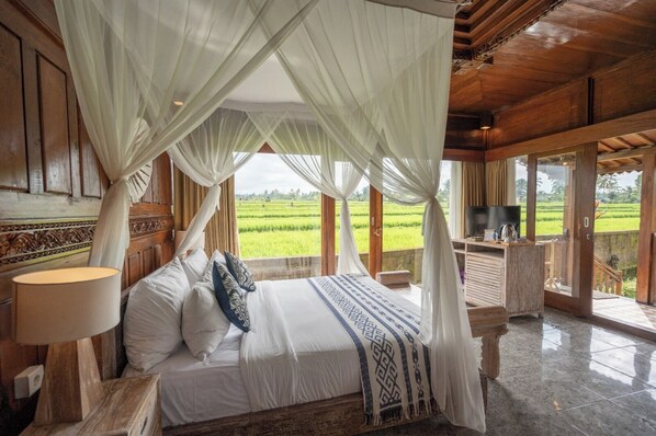 Ein Schlafzimmer mit Baldachinbett, Fernseher und Blick auf Reisfelder.