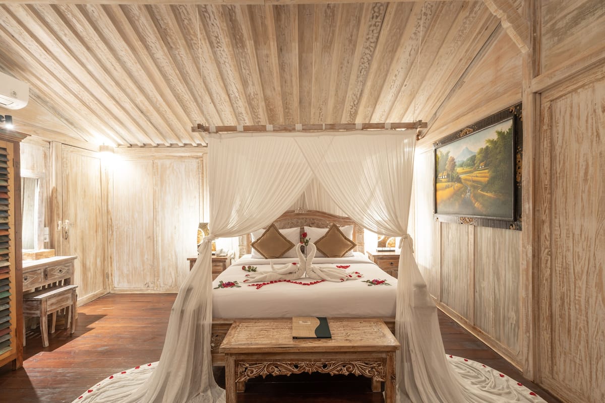 A four-poster canopy bed with a wooden headboard, a bedside table, and a painting on the wall.