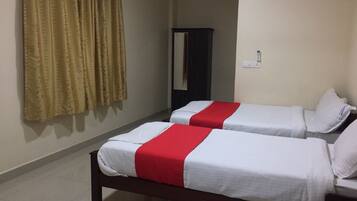 Habitación de hotel con dos camas individuales, cortinas color beige, un armario de madera oscura y un equipo de aire acondicionado en la pared.