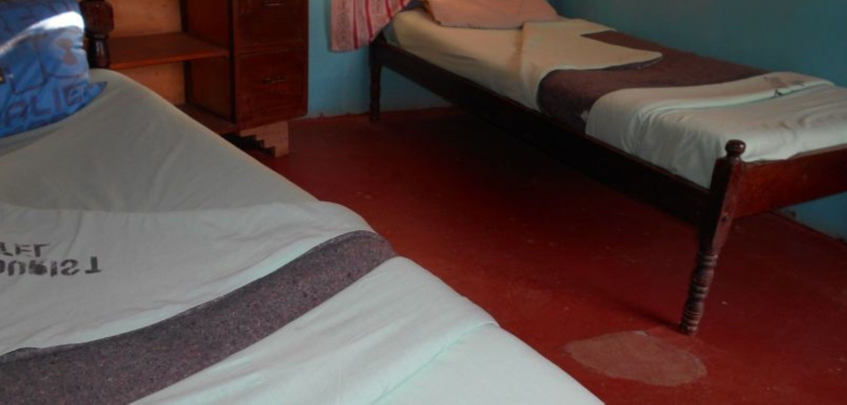 Una habitación pequeña con una cama individual, estructura de madera, suelo rojo y pared azul.