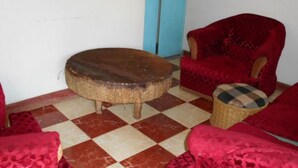A room with a checkered floor, a round wooden table, a red armchair, and a wicker chair with a checkered cushion.