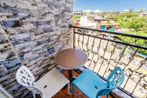 A balcony with a stone wall, a small round table, two chairs, and a view of buildings and greenery.