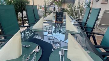 Une table dressée pour un repas en plein air, avec des chaises vertes, une table en verre et un panneau indiquant le menu.