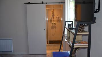 Una habitación con una puerta corredera que da a un baño, una pequeña mesa con un jarrón, y una estantería con libros y objetos decorativos.