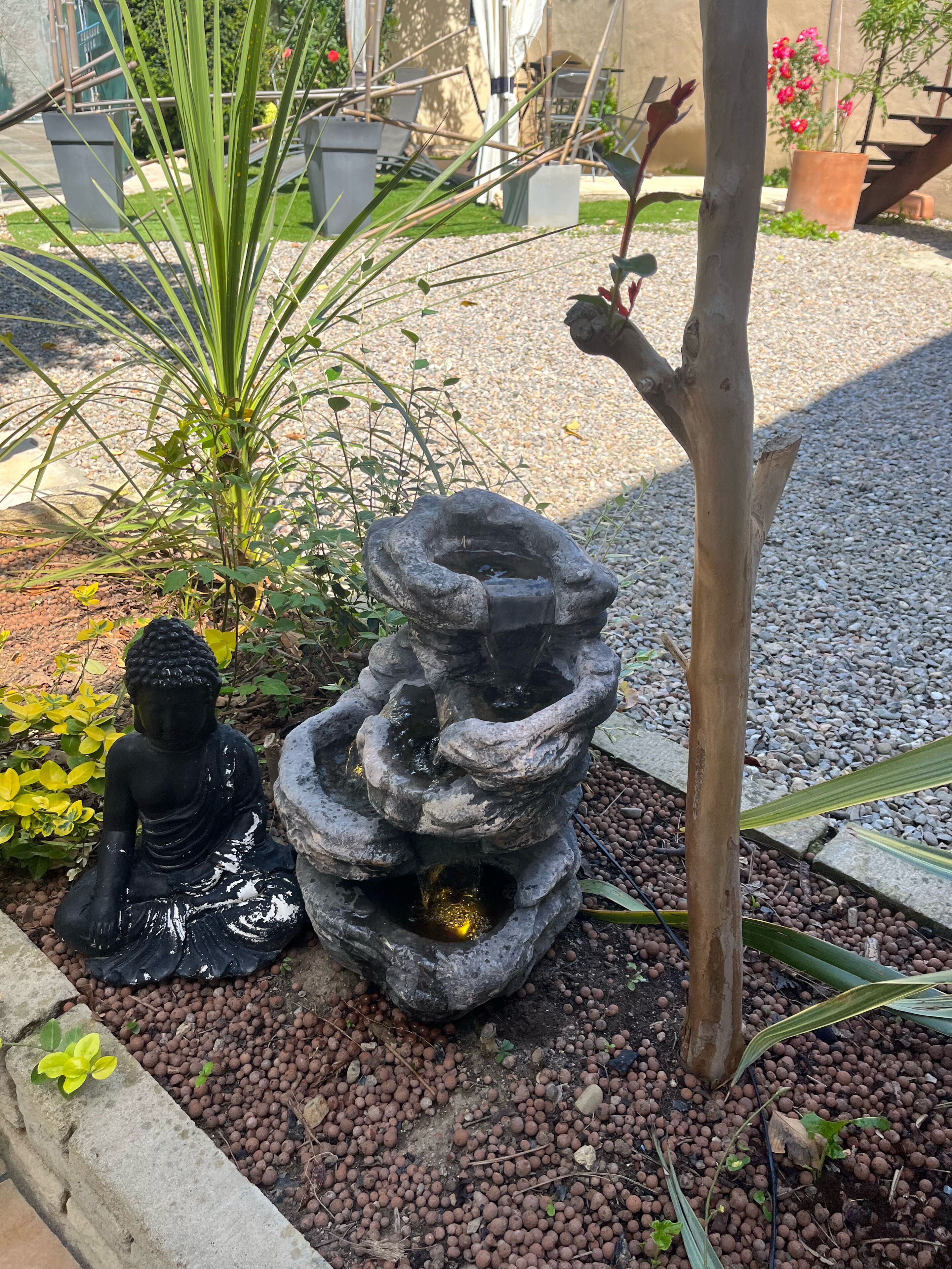 Un giardino con una statua di Buddha, una fontana di pietra e un albero.
