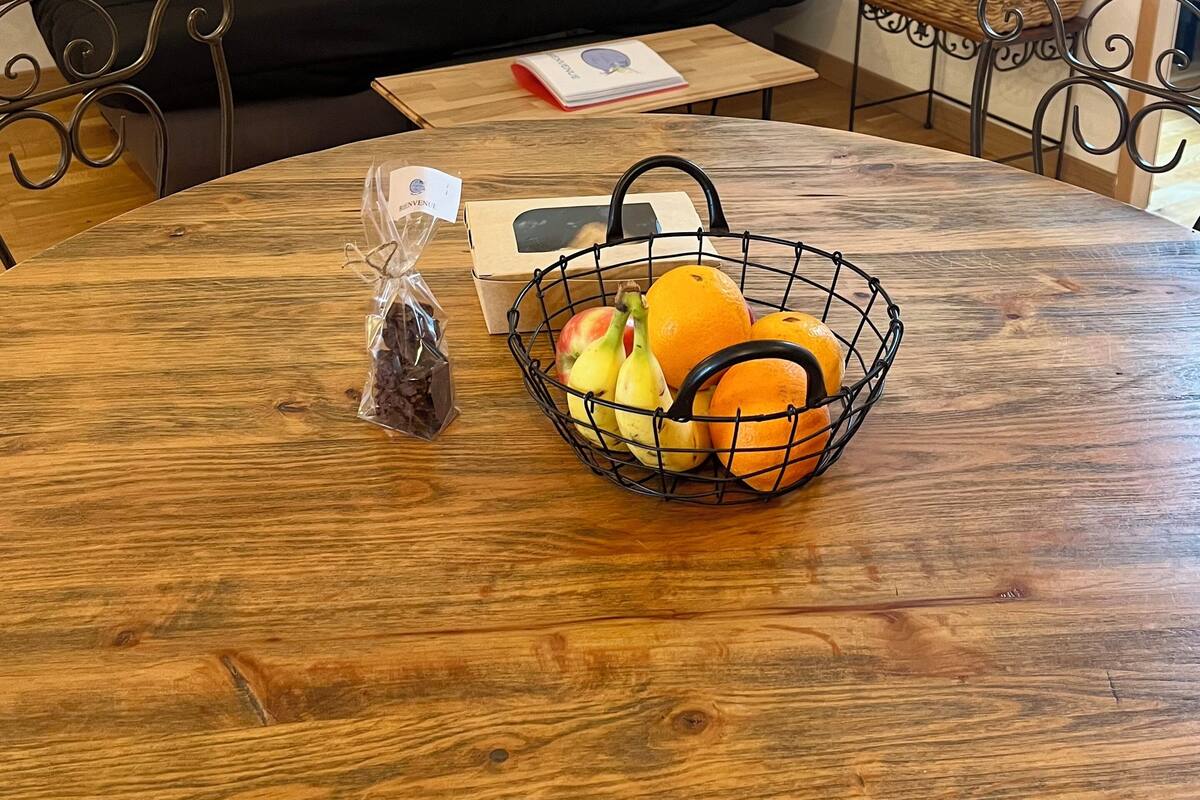 A dining table with a fruit basket, a box, and a bag of snacks.