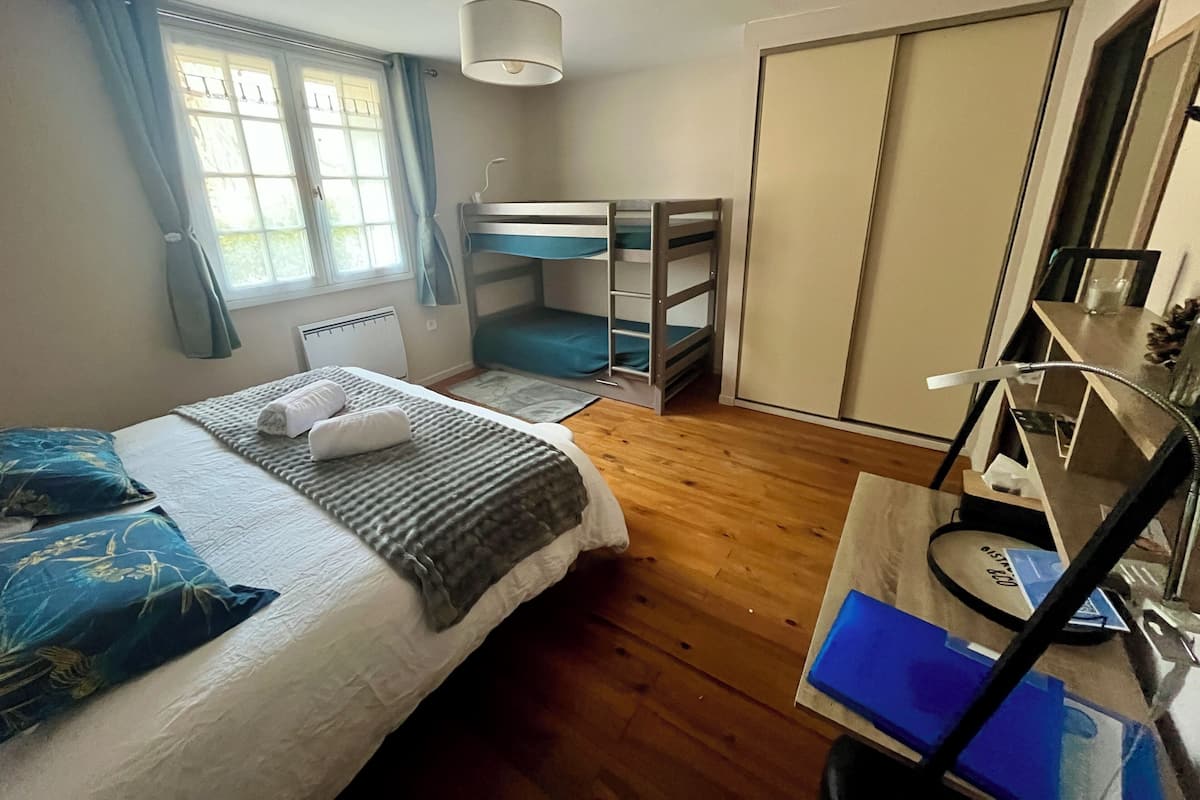 A bedroom with a bunk bed, a desk with a chair, a radiator, and a window with curtains.