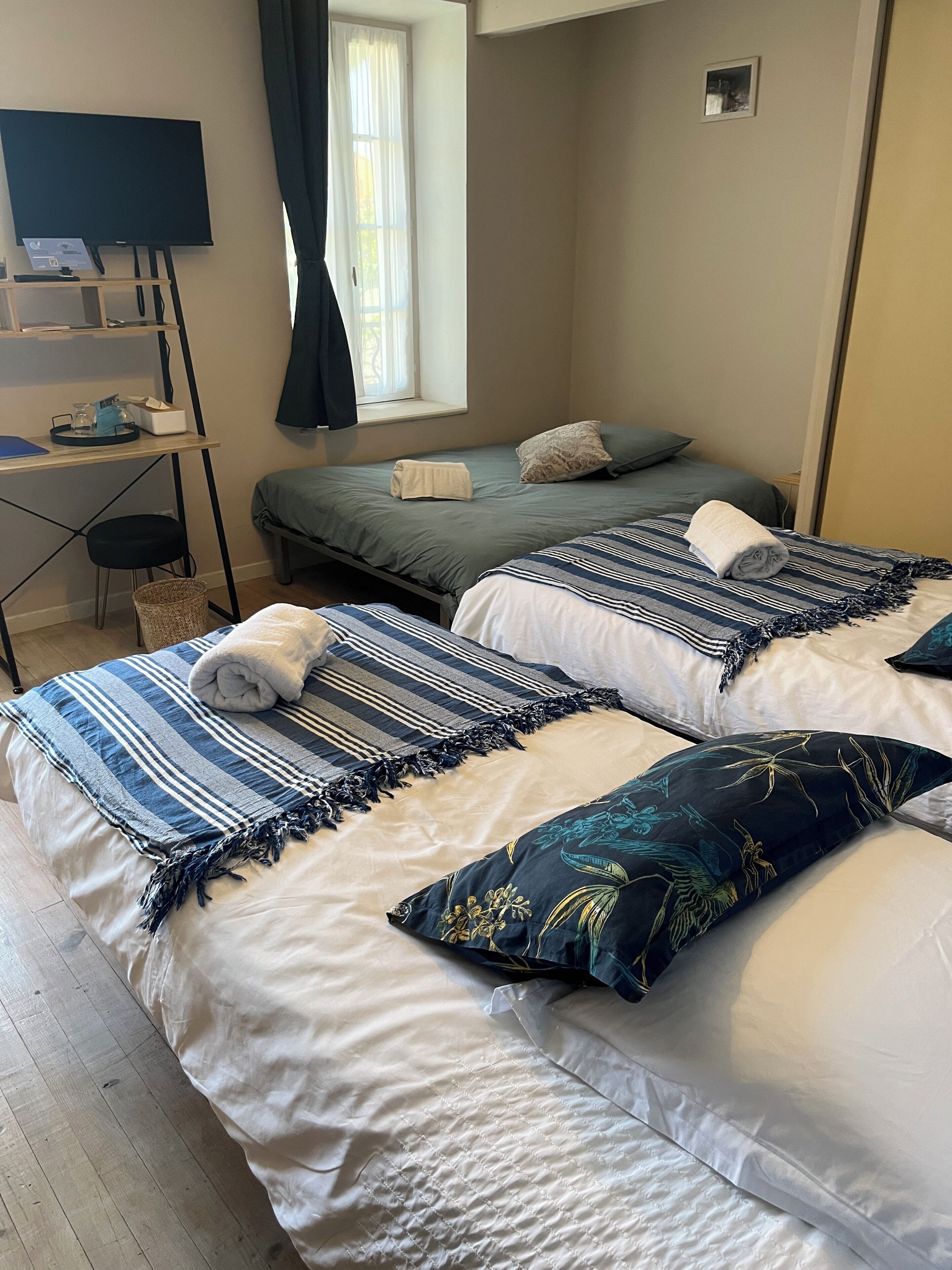 Quarto de hotel com duas camas, uma escrivaninha, televisão e janela com cortinas.