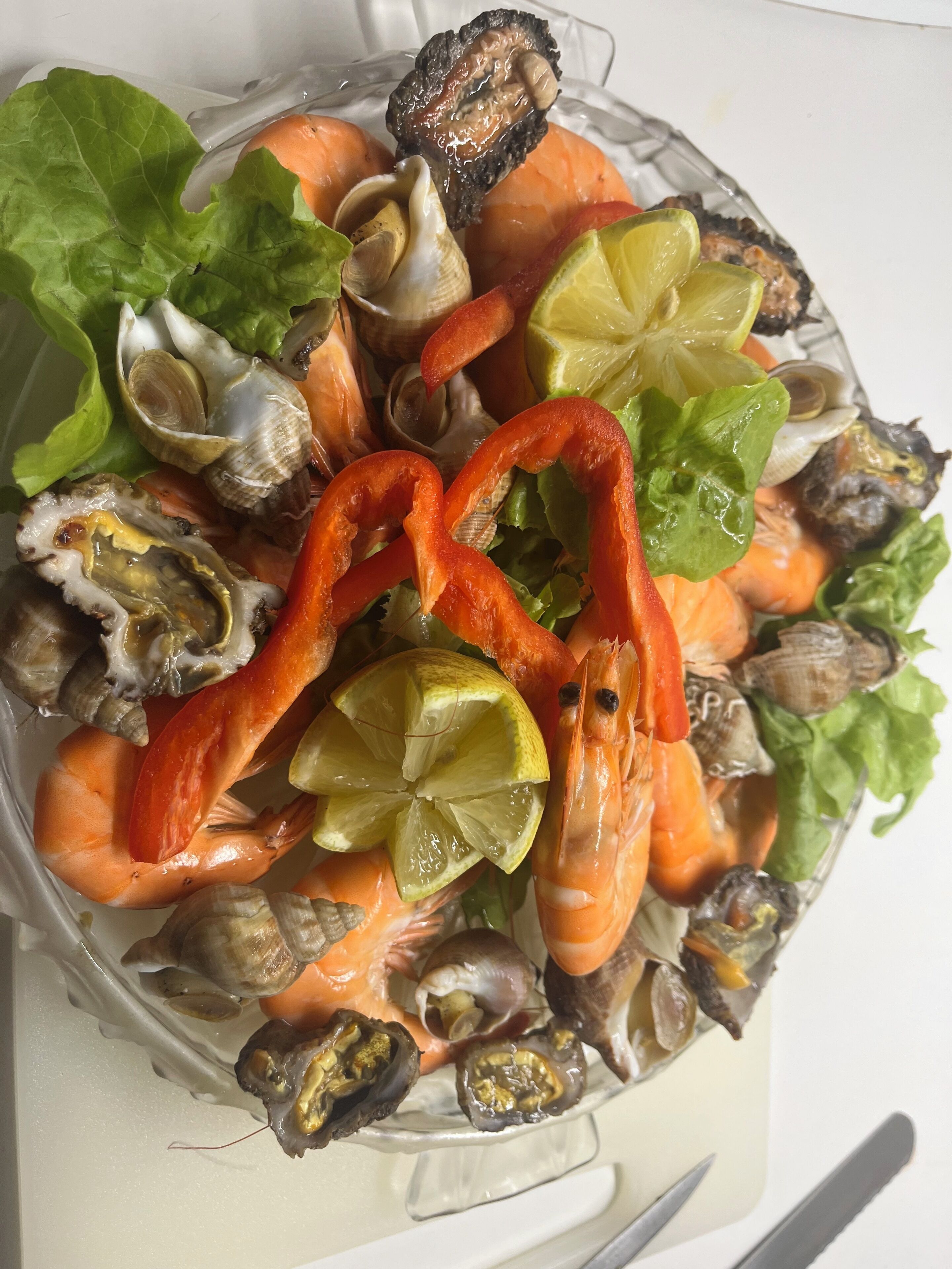 A seafood platter with shrimp, clams, and oysters, garnished with lime and lettuce.