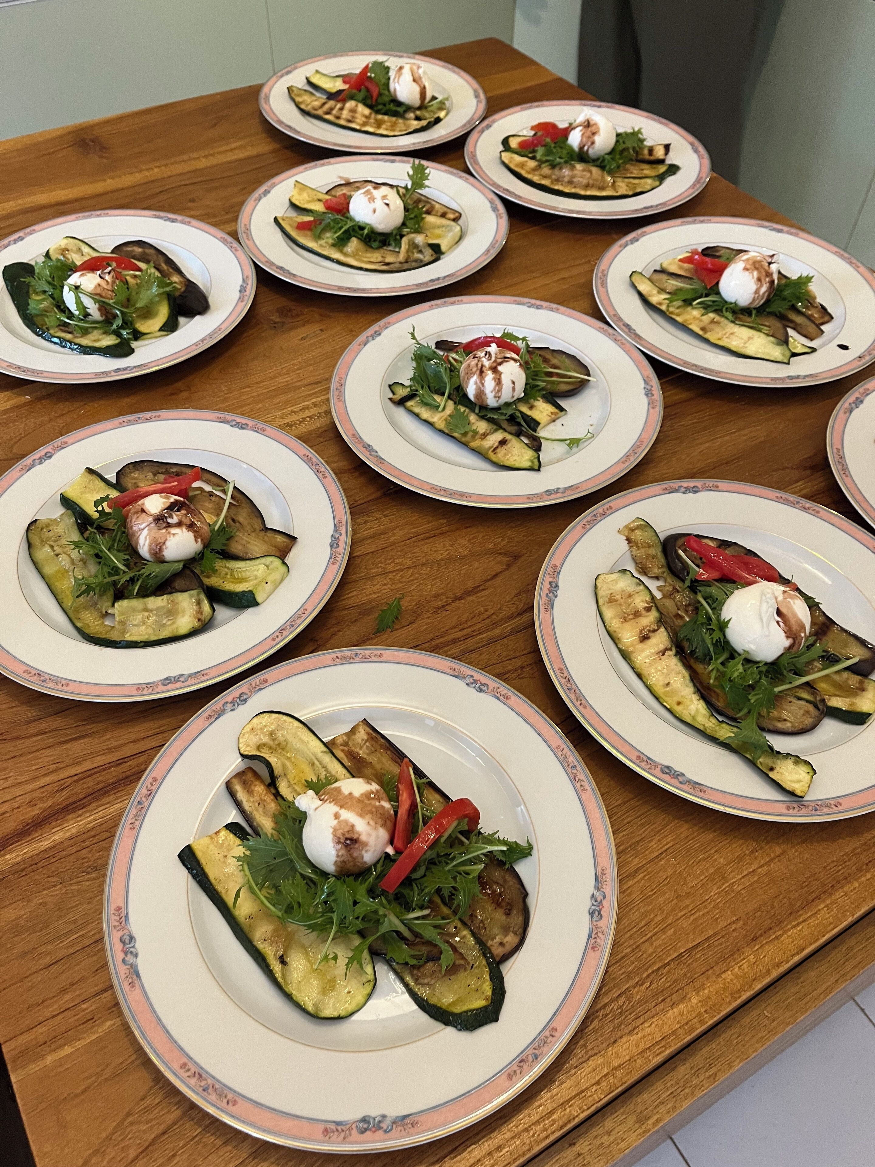 A wooden table with multiple plates of grilled vegetables and a poached egg on each.