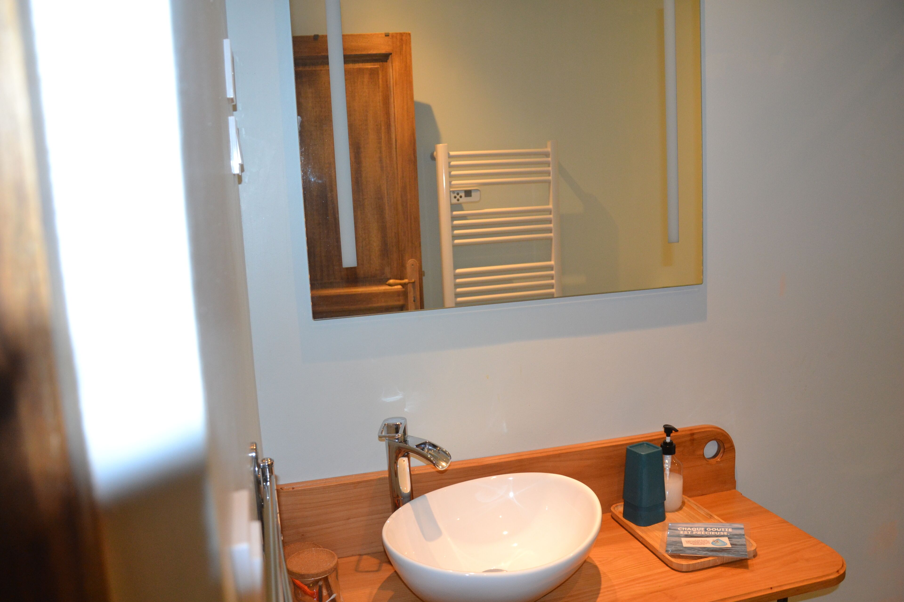 A bathroom with a white sink, a wooden vanity, a mirror, and a towel rack.