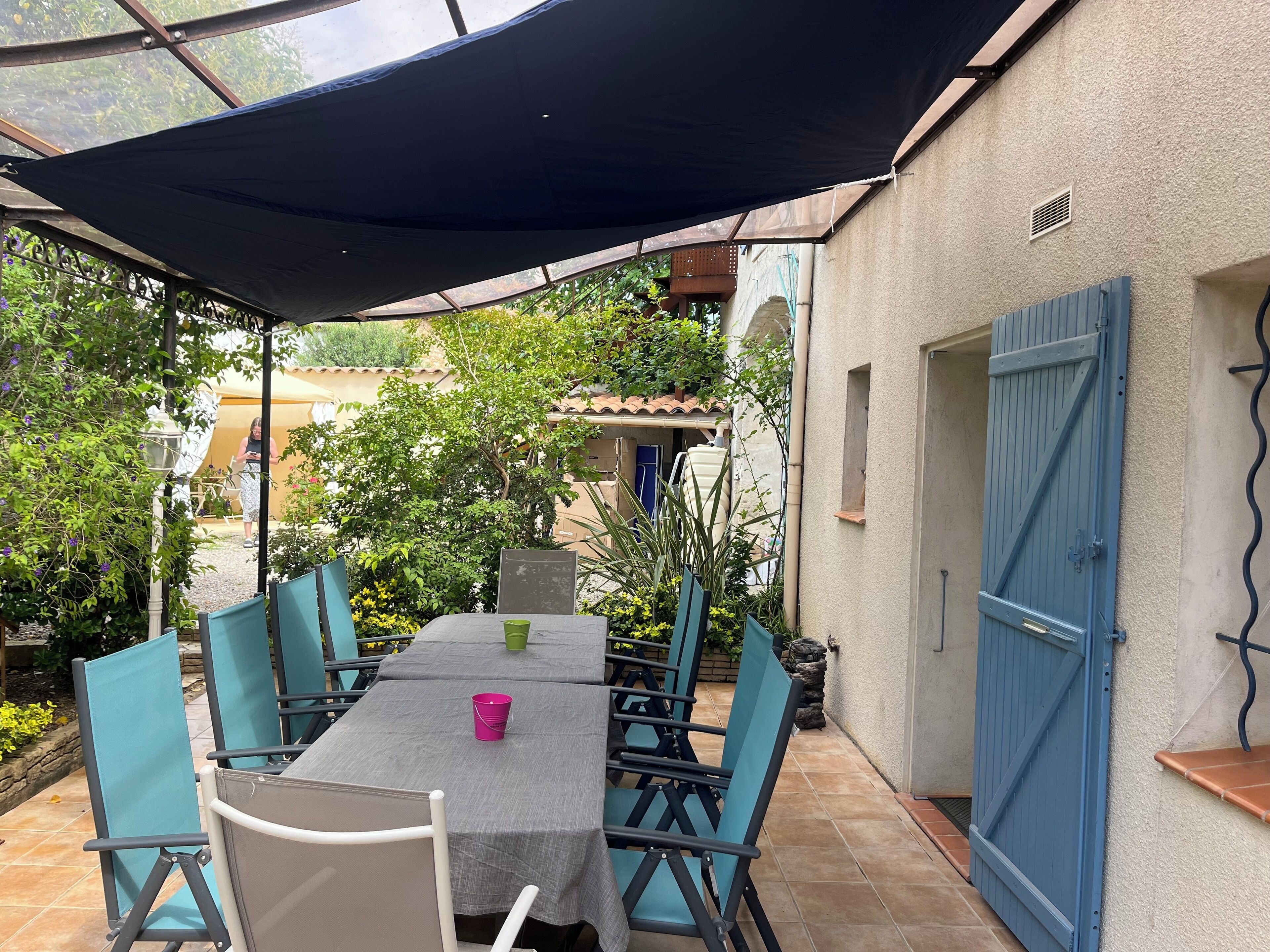 Un patio al aire libre con una mesa, sillas, un área cubierta y una verja azul.